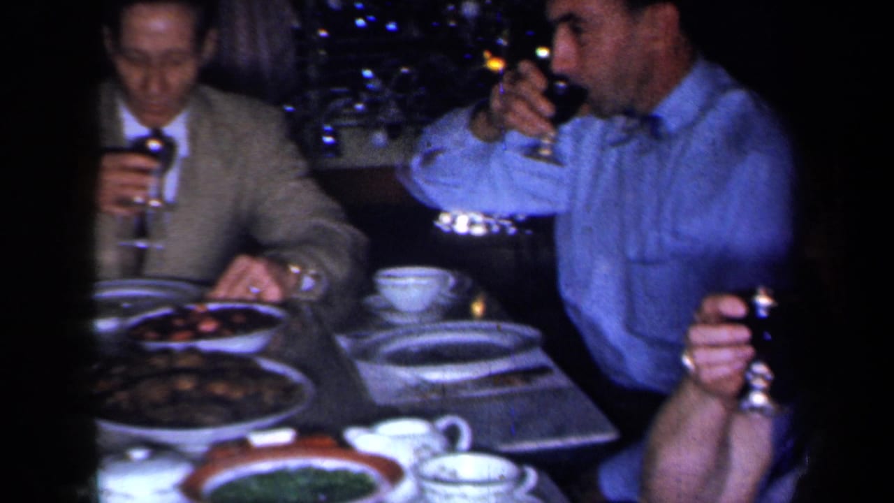Adults seated at a dinner table with wine glasses, plates, cups, and serving dishes.