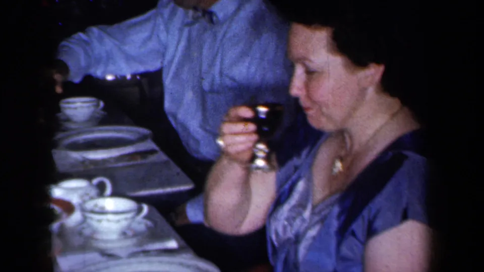 1959 New York dinner-party frame with a woman holding a drink beside patterned china and table settings.