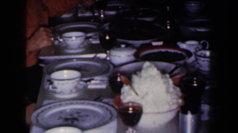 1959 New York home-movie frame showing a dimly lit formal table with drinks, china, and serving dishes.