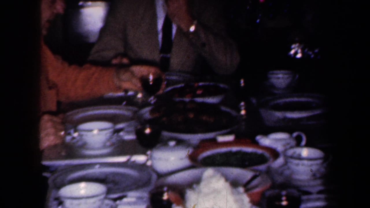 Adults seated around a dining table with cups, saucers, plates, and serving dishes.