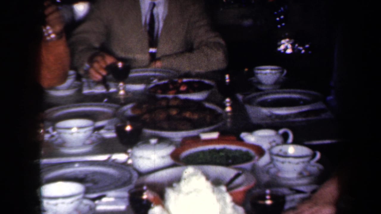 Formal dining table with adults, china place settings, cups, serving dishes, and dim interior lighting.