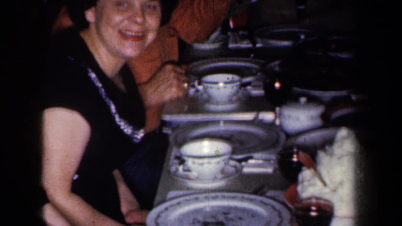 Smiling woman in a dark dress seated at a crowded formal dining table with china and glasses.