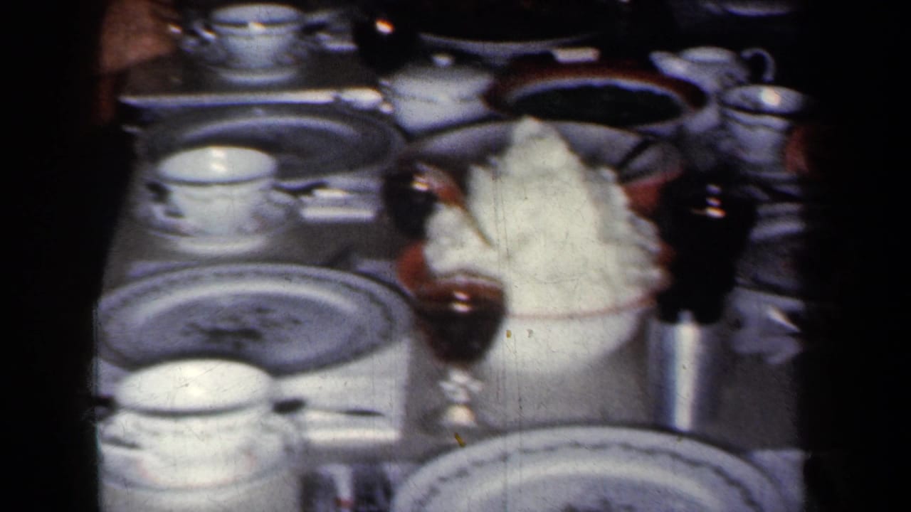 1959 New York home-movie frame focused on tableware and food, including patterned plates, teacups, silverware, a drink glass, and mashed potatoes.