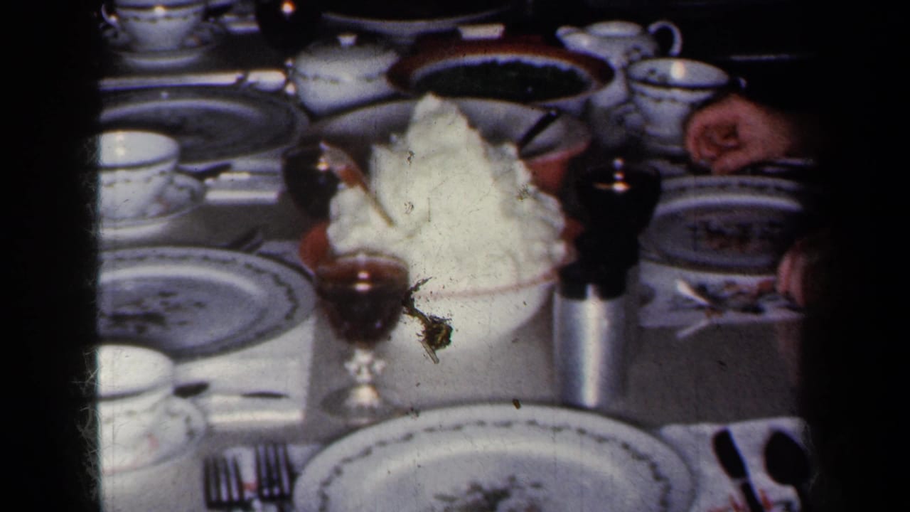 1959 New York home-movie frame showing a formal dinner table with patterned china, cups, wine glasses, and a central serving of potatoes.
