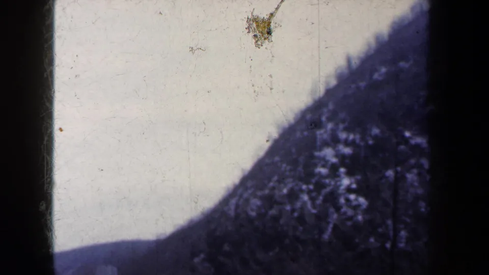 1959 New York 8mm frame showing a dark mountain ridge against pale sky, with dust marks and the rounded edge of the film gate.