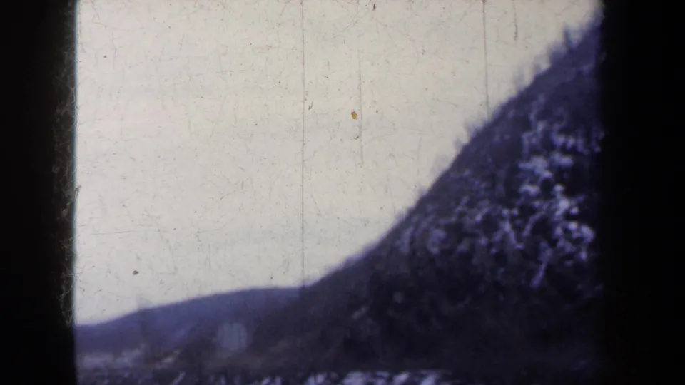 1959 New York 8mm frame showing a snowy hillside and riverbank under overcast light, with visible film gate edges.