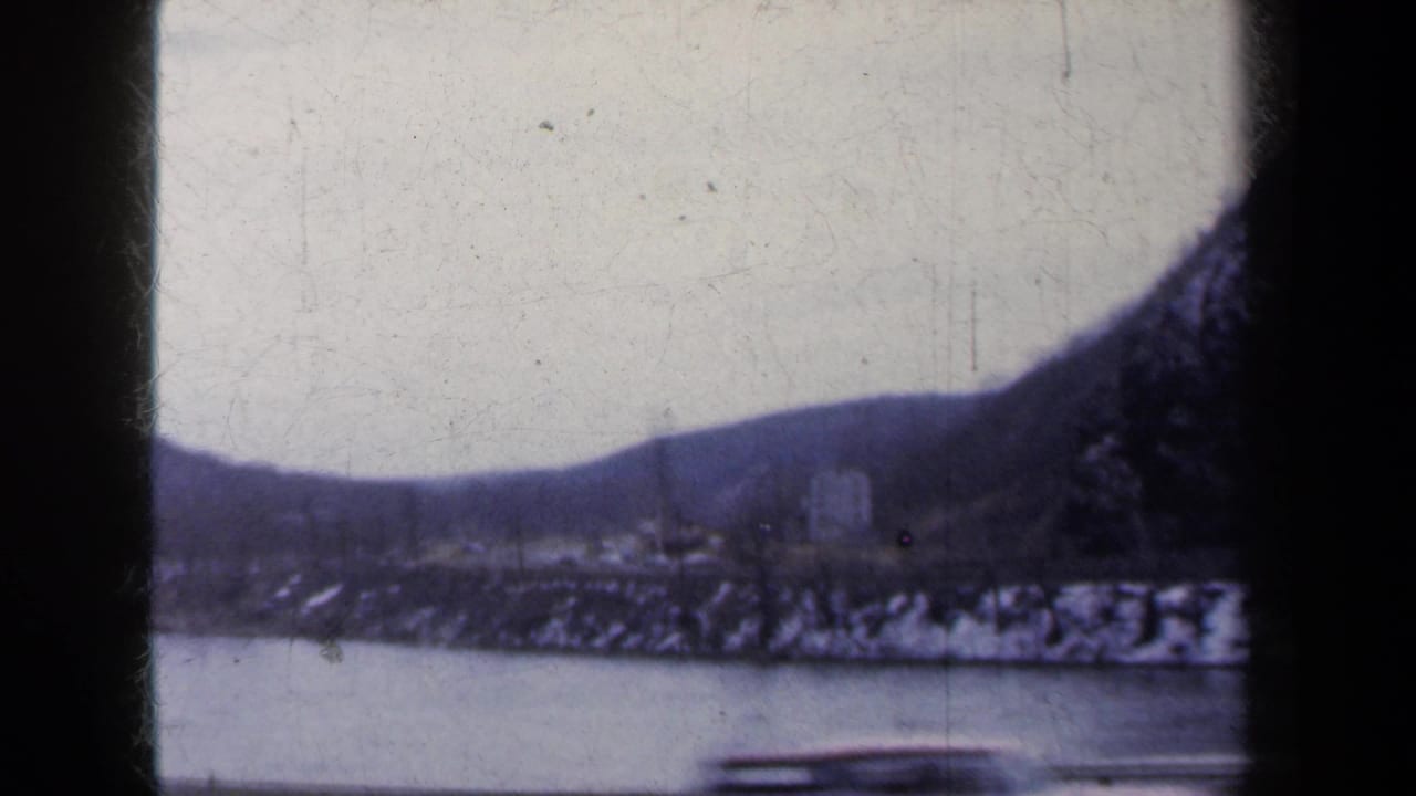 A faded 8mm view of a New York river valley in winter, with snow patches on the bank and hills in the distance.