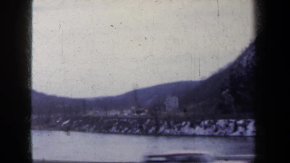 A faded 8mm view of a New York river valley in winter, with snow patches on the bank and hills in the distance.