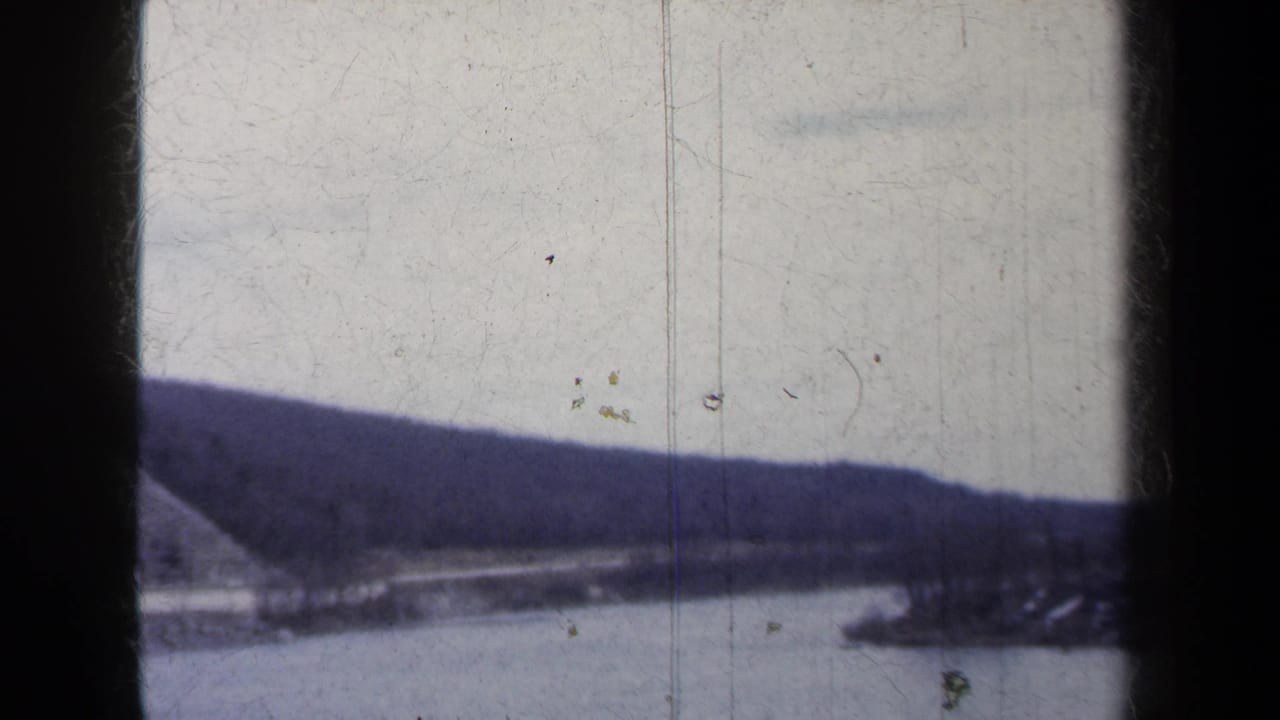 Lake and forested mountain viewed from a moving roadside vantage.