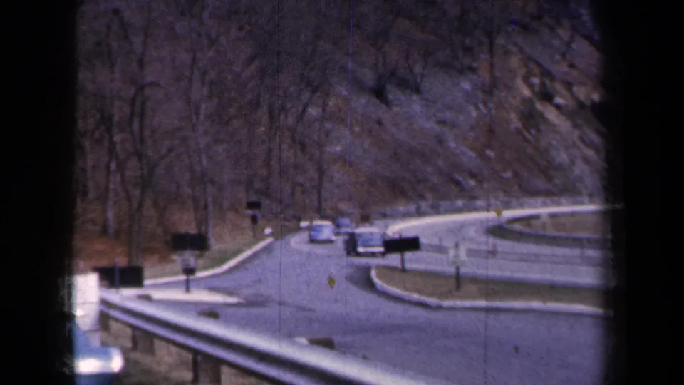 1959 New York frame showing cars on a winding mountain road viewed through dark film or window-frame edges.