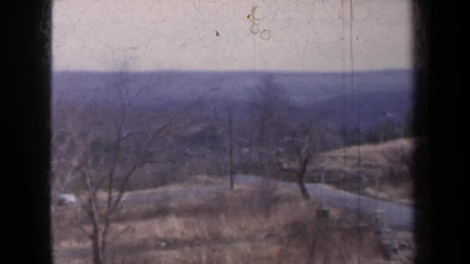 1959 New York 8mm view of bare trees, a curving rural road, utility poles, and muted hills under a pale sky.
