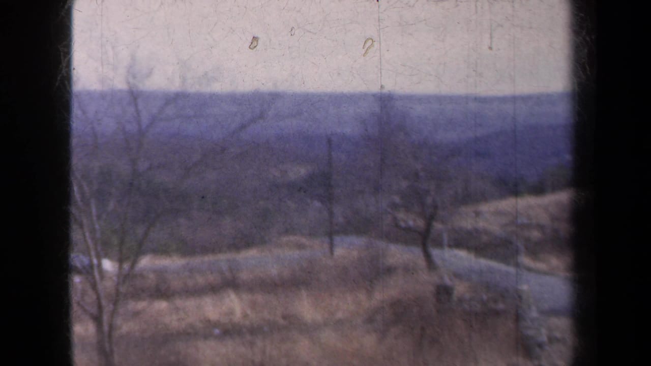 Rural hills and bare trees seen through a dark vehicle window frame.