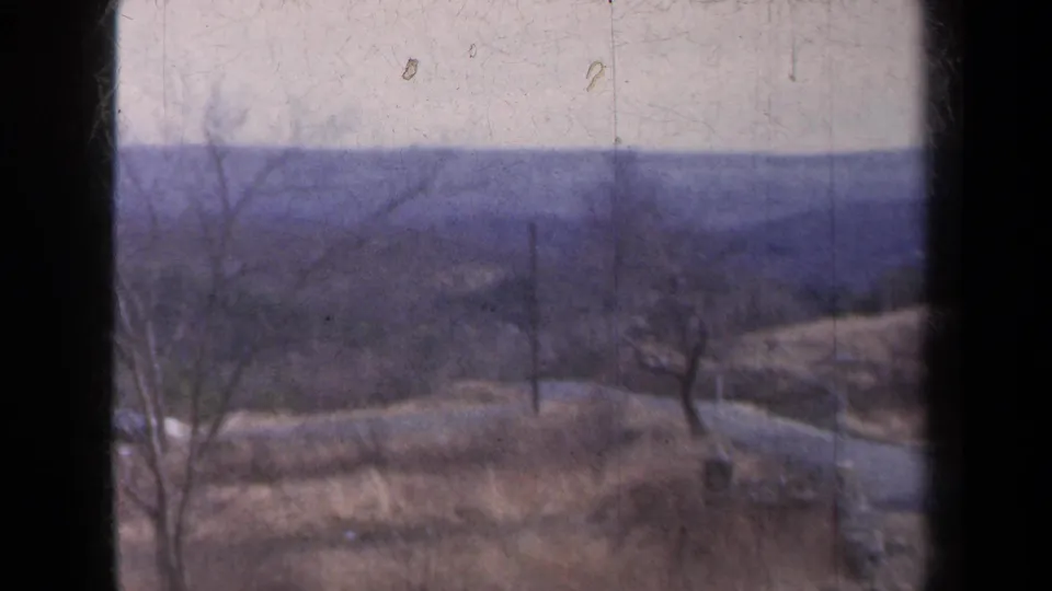 1959 rural New York landscape viewed from inside a moving vehicle, with bare trees, low hills, and a pale sky.