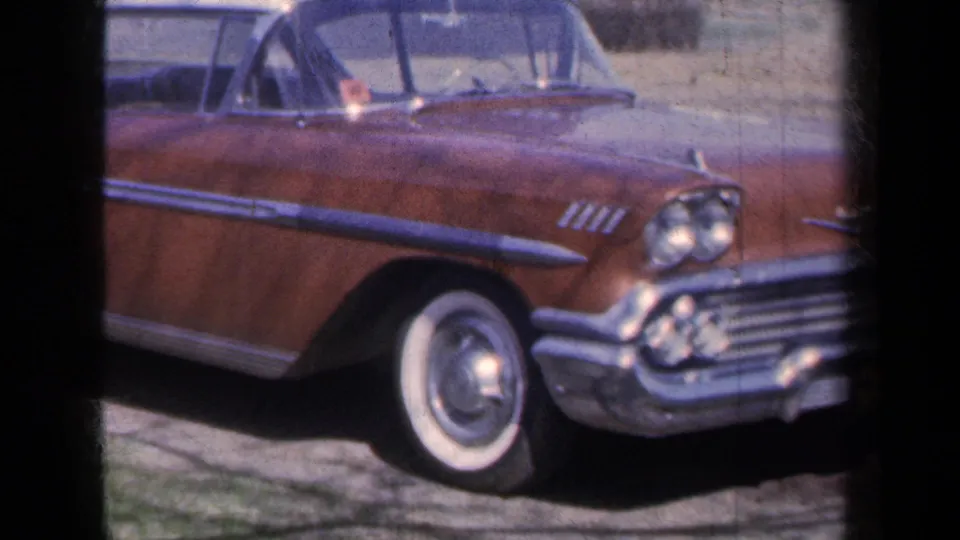 The parked brown Chevrolet convertible is shown closer, with whitewall tire, chrome bumper, grille, and fender details.
