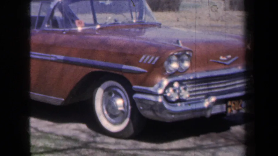 1959 red Chevrolet Bel Air convertible in New York, seen from the front side with chrome grille, dual headlight, and whitewall tire on 8mm film.