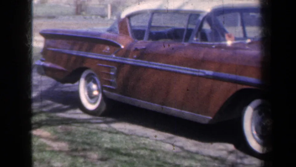 1959 New York home-movie frame showing a wood-paneled station wagon with chrome trim and whitewall tires in a suburban driveway.