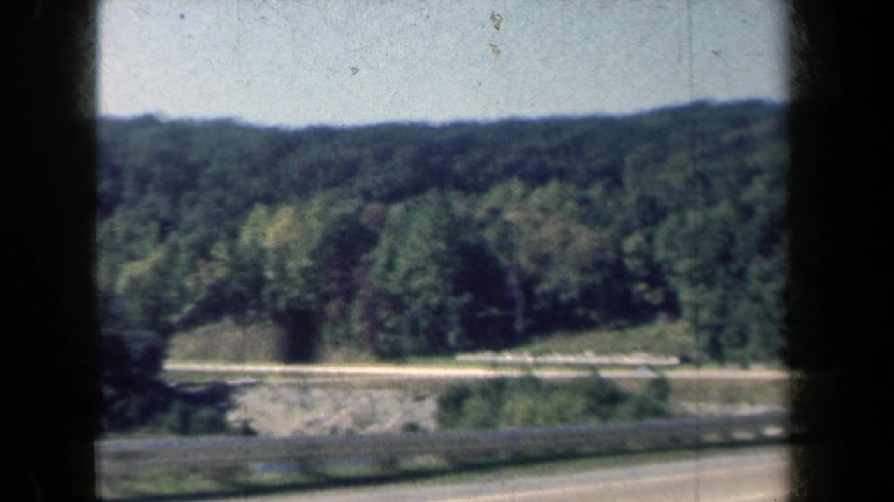 Wooded New York roadside and hillside appear through dark frame edges in this 1959 8mm travel shot.