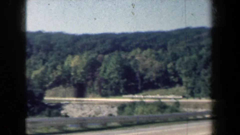 Wooded New York roadside and hillside appear through dark frame edges in this 1959 8mm travel shot.