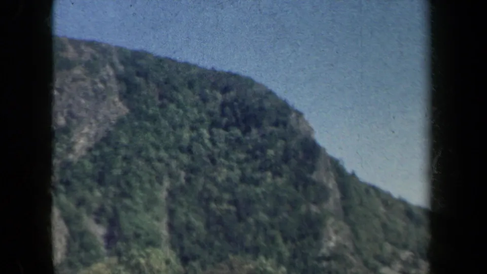 A steep wooded hillside or rock face rises beside the New York roadway in this 1959 home-movie frame.