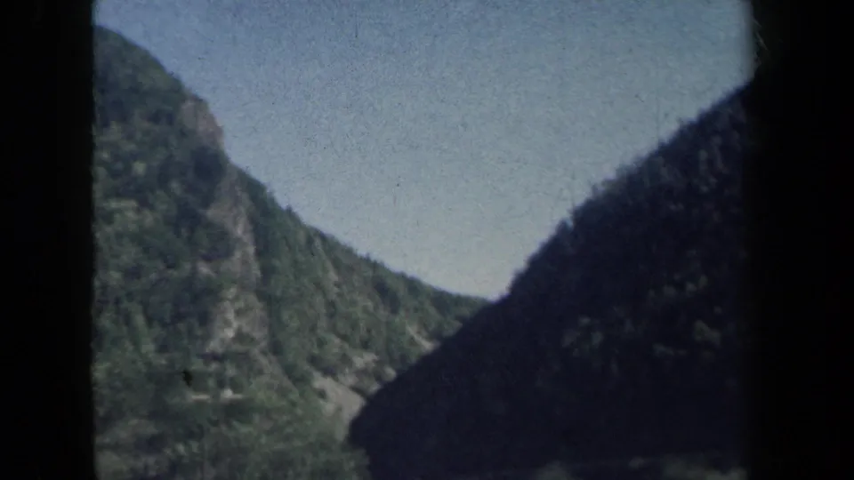 Passenger-side view of a green mountain ridge in New York, with dark car-window framing and 8mm grain from the 1959 footage.