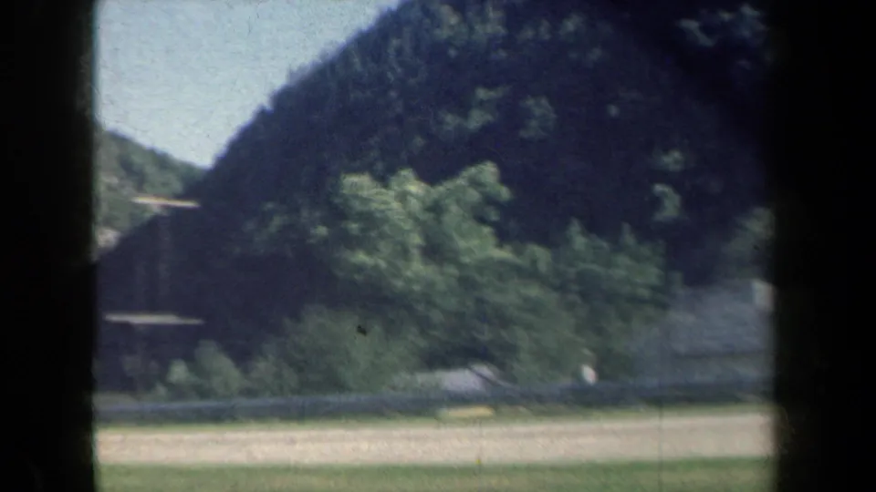 Moving 8mm view of a rural New York roadside valley, with wooded hills, utility poles, and road edges passing below the mountains.