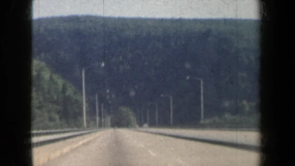 1959 New York 8mm view from a moving car on a divided freeway through forested hills.