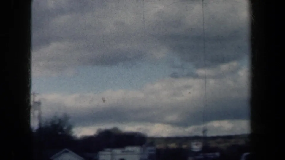 Soft 8mm travel frame from 1959 New York showing cloud cover, distant hills and blurred roadside edges.