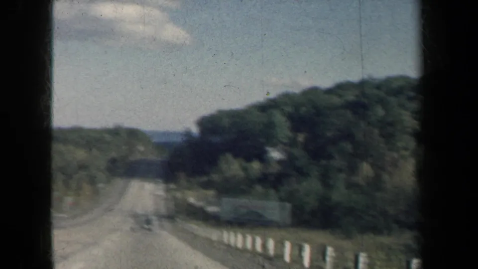 1959 New York home-movie frame looking down a tree-lined highway from a moving vehicle.
