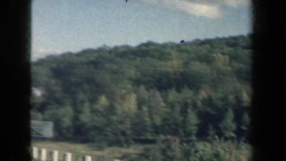 1959 New York home-movie frame showing wooded hills and a roadside view from a moving vehicle.