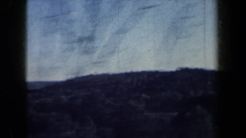 1959 New York home-movie frame with distant wooded hills under a pale sky, softened by 8mm exposure.