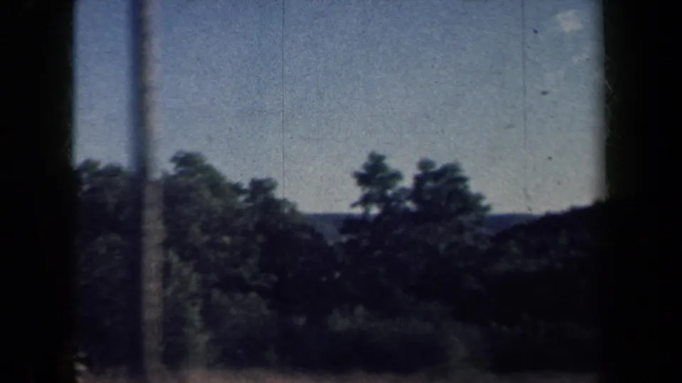 Passenger-side 8mm view of rural New York trees and low hills under a bright sky in 1959 footage.