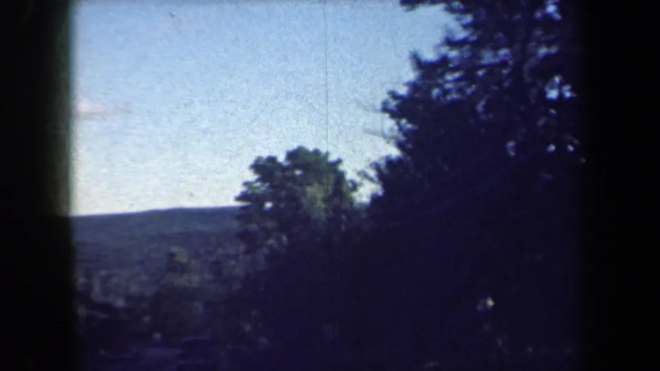 Late-1950s 8mm view of a wooded rural New York roadside with hills beyond and strong dark frame borders.
