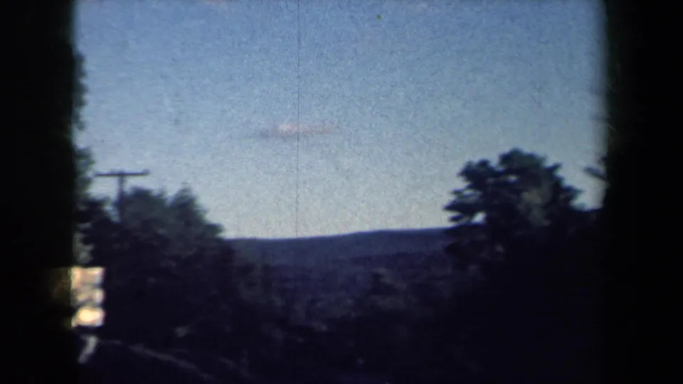 1959 8mm rural New York road view with wooded hills, blue sky, dark frame edges, and a utility pole near the roadside.