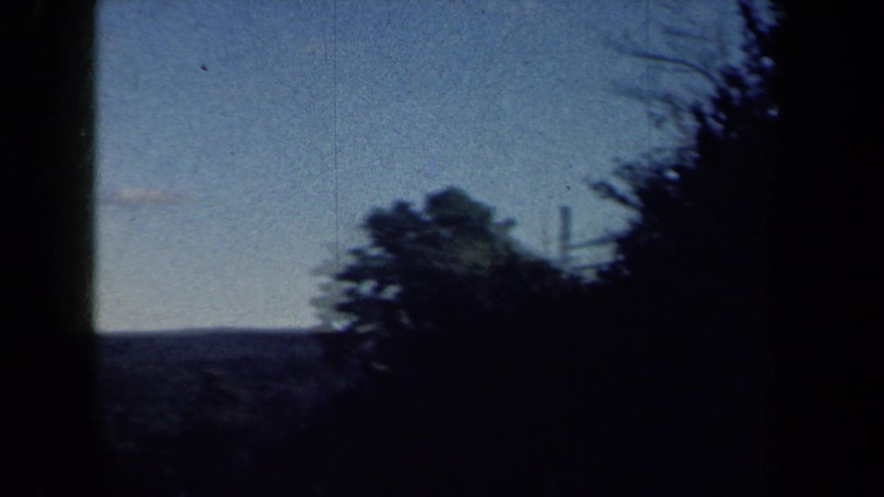 Rural New York landscape from the moving 8mm camera, with distant hills, trees, sky, and overhead utility lines.