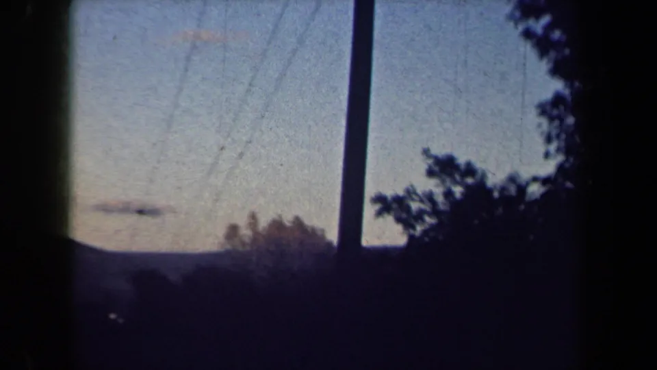 1959 New York home-movie frame showing a dim sky crossed by utility lines with a pole and silhouetted trees in the foreground.