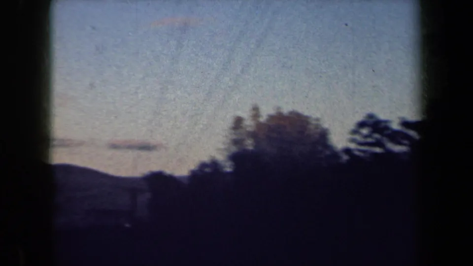 1959 New York 8mm frame with a pale evening sky, low dark trees, and a blurred foreground from the moving camera.