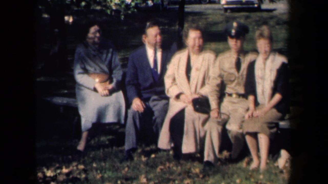 Five people sit on a New York park bench, including a suited man and a young person in a military-style uniform.