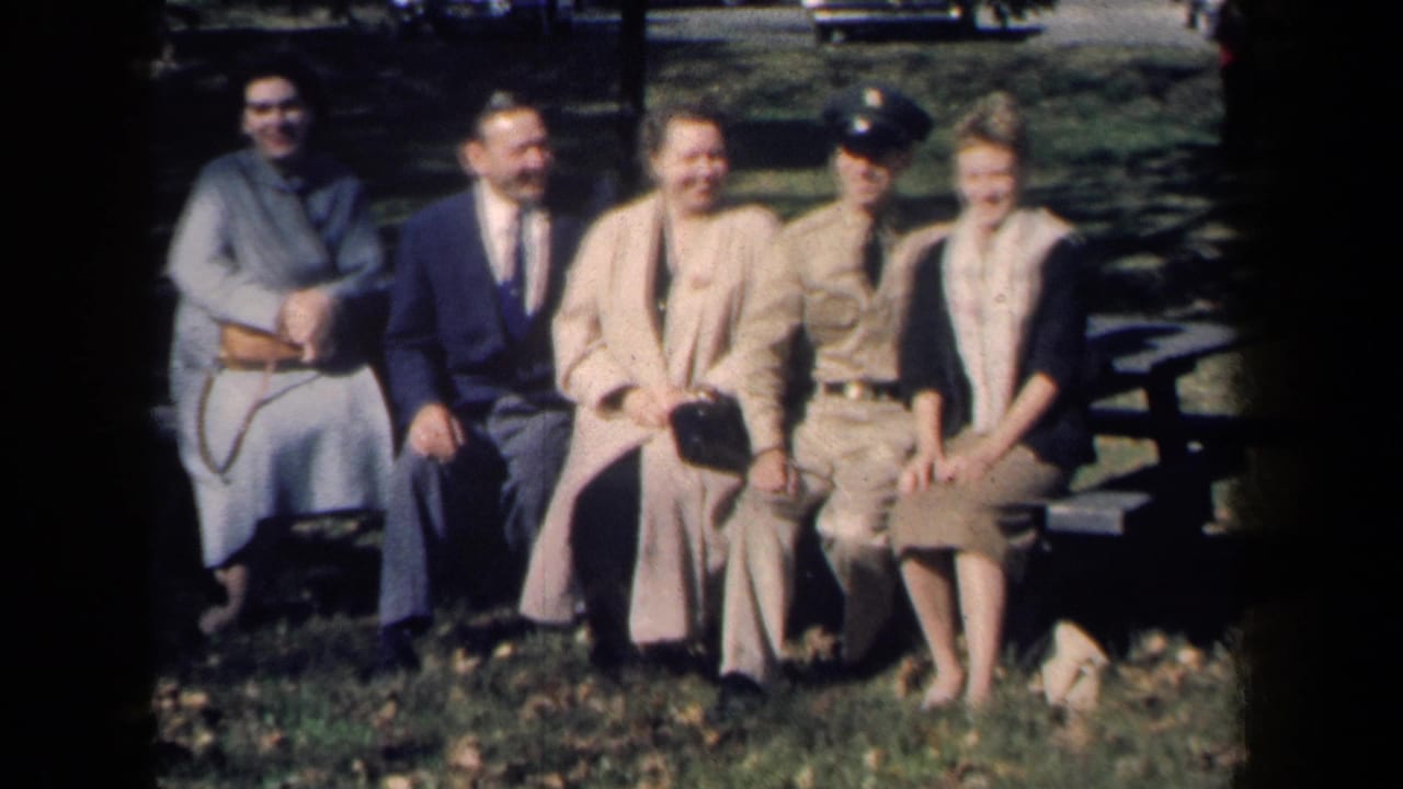 Five adults sitting on a park bench, including a uniformed man and people in coats.