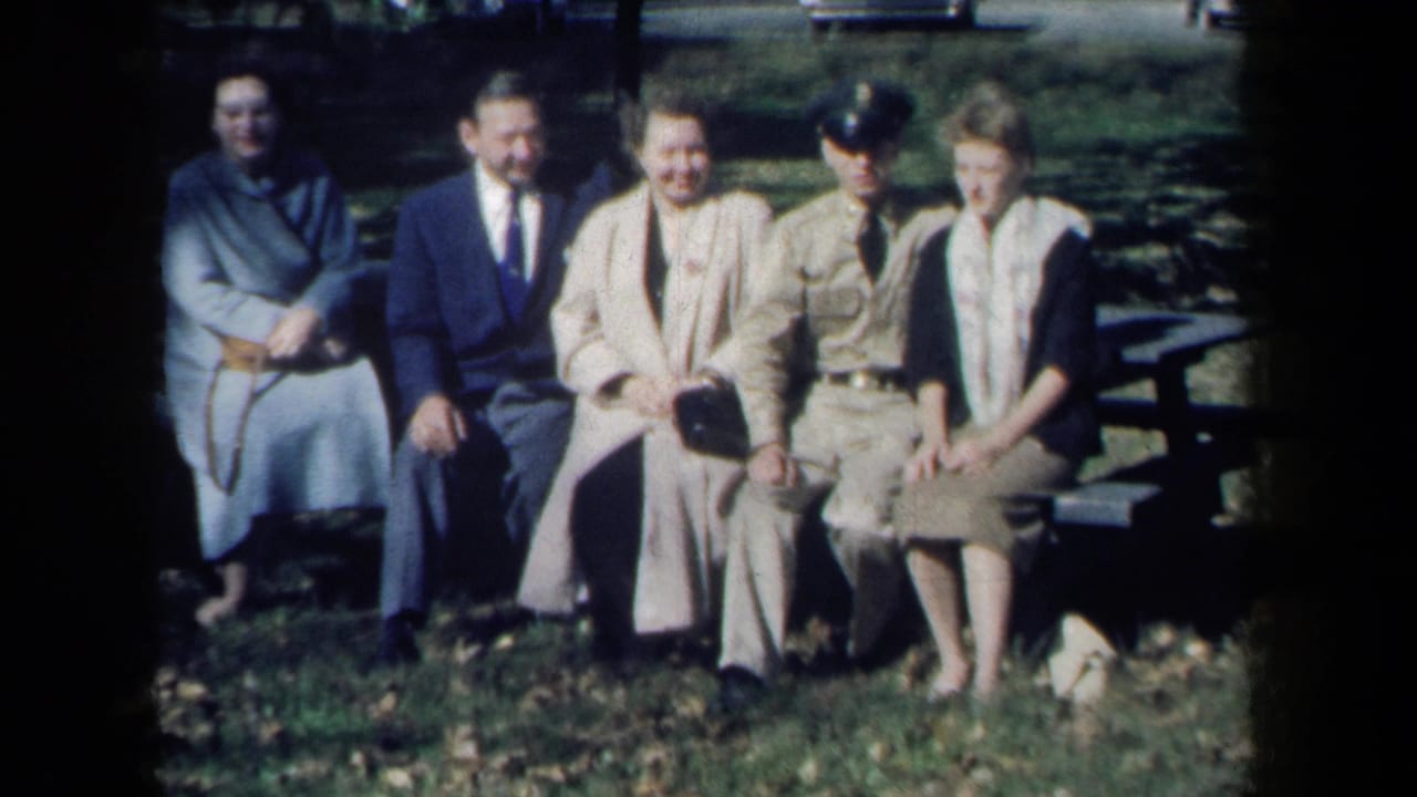1959 New York park scene with adults seated together on a bench, one in uniform, captured in soft color 8mm footage.