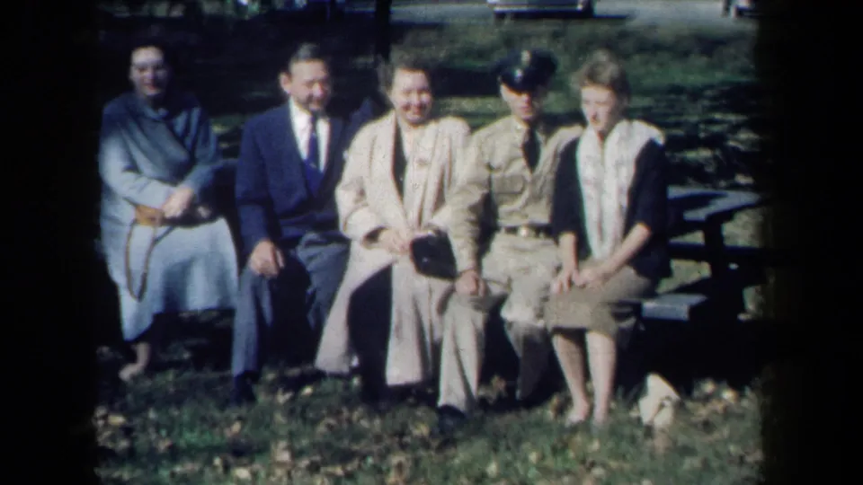 1959 New York park scene with adults seated together on a bench, one in uniform, captured in soft color 8mm footage.