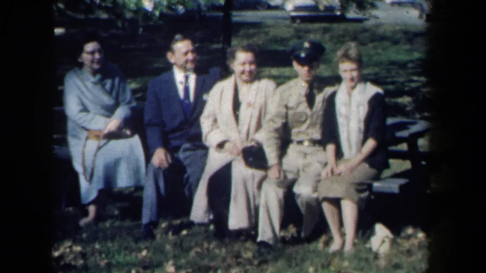 A 1959 New York 8mm frame shows a family or social group on a park bench, with mid-century clothing and a uniformed man visible.