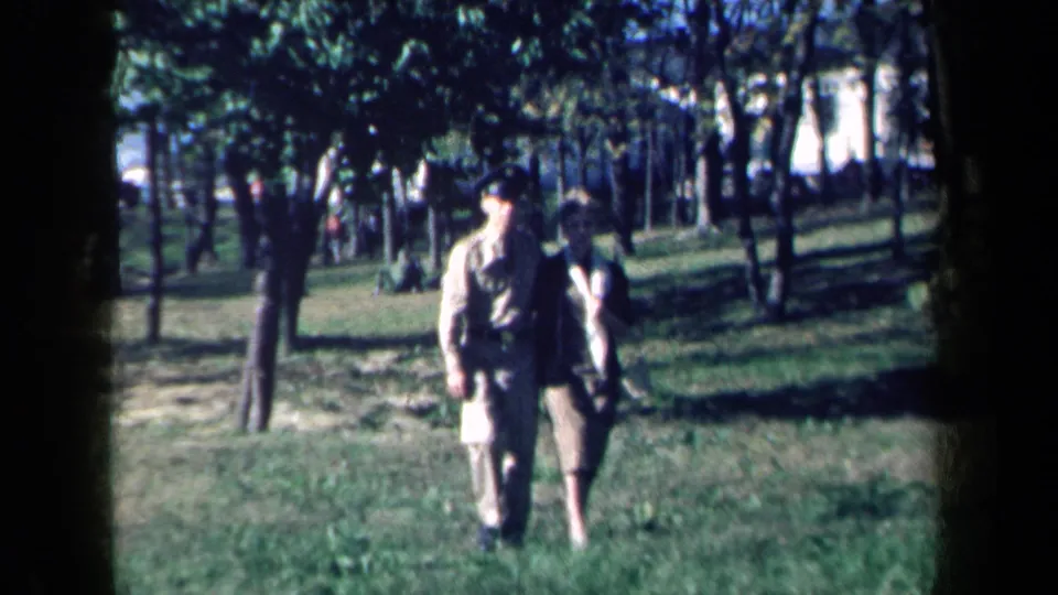 A couple walks arm in arm toward the camera in a grassy New York park, with the 8mm frame showing grain and dark edge vignetting.