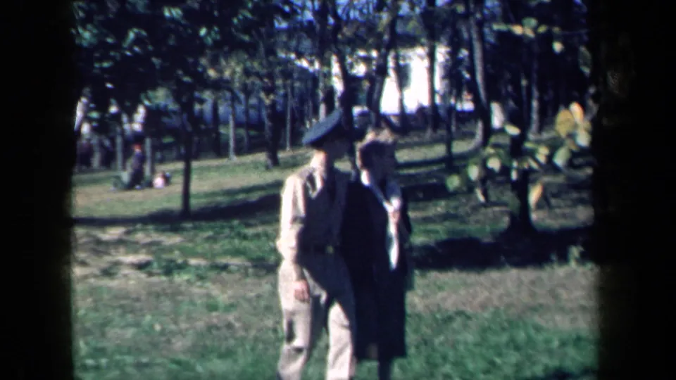 In 1959 New York home-movie footage, a uniformed man and woman walk together across a sunlit park lawn.