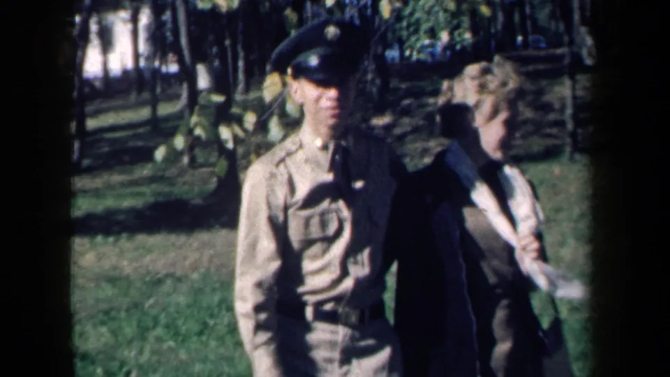A closer 8mm frame shows the uniformed man and woman walking together in the 1959 New York park scene.