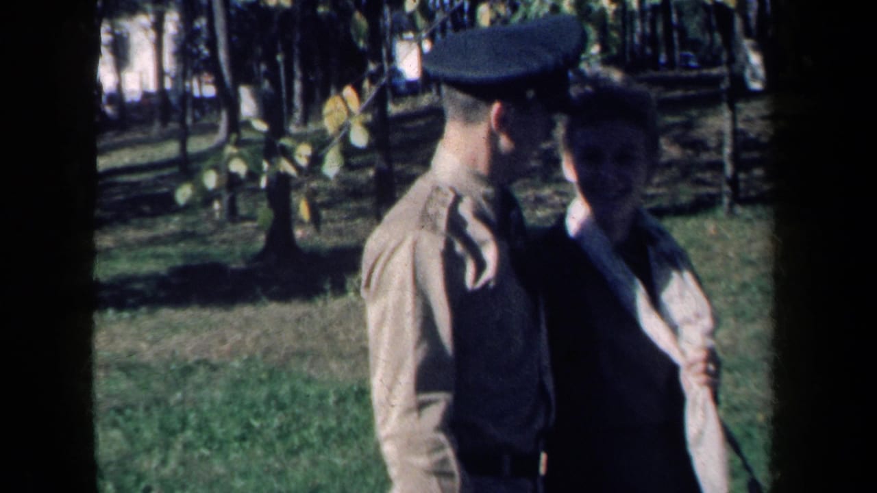 The couple remains arm-in-arm in the 1959 New York park footage, with trees and a rustic fence behind them.