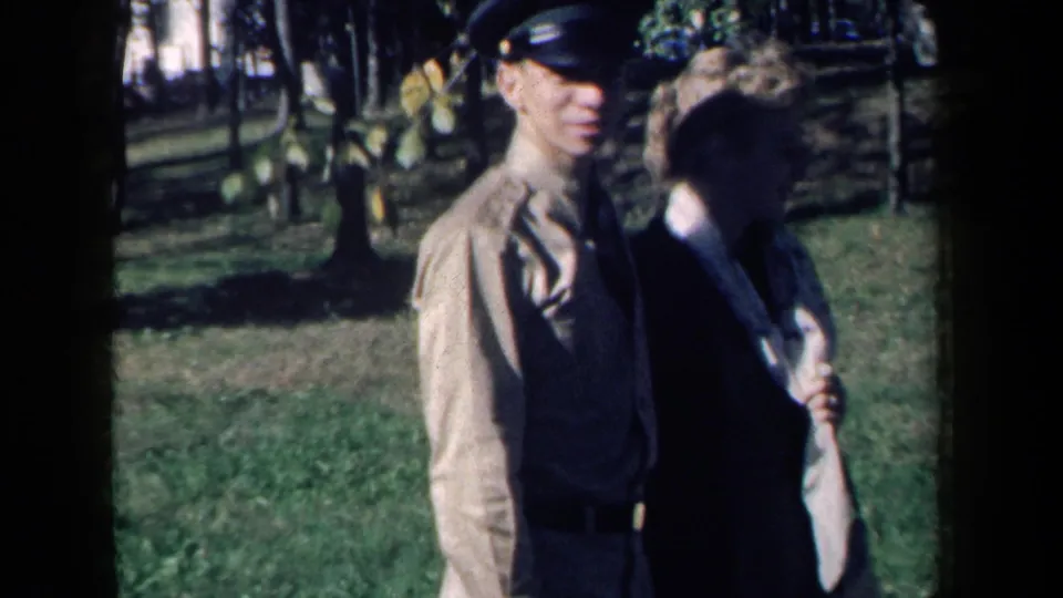 A smiling young man in uniform walks with a woman through a grassy New York park in 1959 home-movie footage.