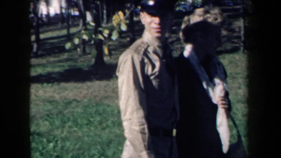 In supported 1959 New York home-movie footage, a man and woman stand on a grassy lawn near trees in bright daylight.