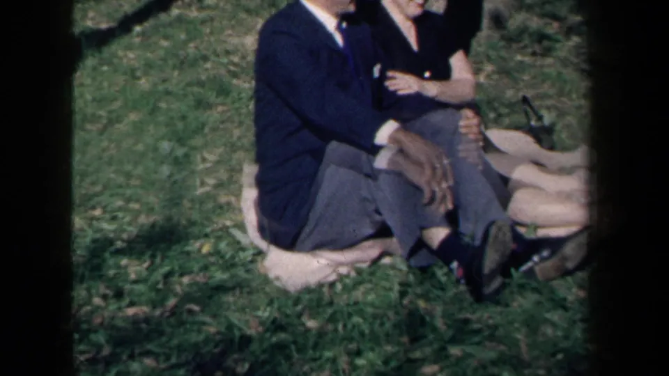 A closer cropped frame shows the seated couple's dark clothing, crossed legs, blanket, and grassy park setting.