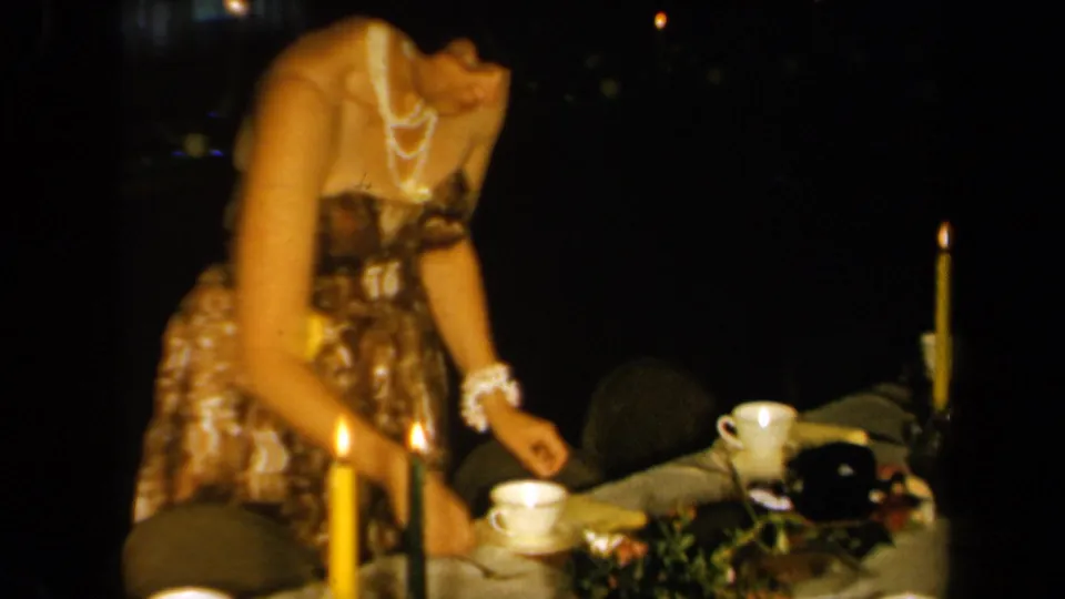 1961 California home-movie frame of a woman serving or arranging a candlelit dinner table in a dark interior.