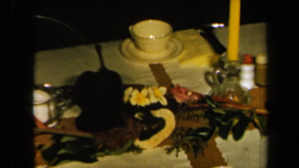 A close table view shows a lit candle, teacup, tropical flowers, serving pieces, and decorations from the dim indoor party setup.